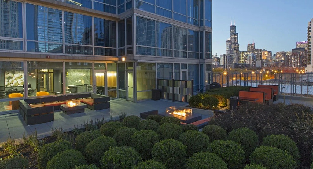 Luxurious rooftop terrace at 1401 S. State Apartments in Chicago, featuring fire pits, lounge seating, and a stunning city skyline at dusk