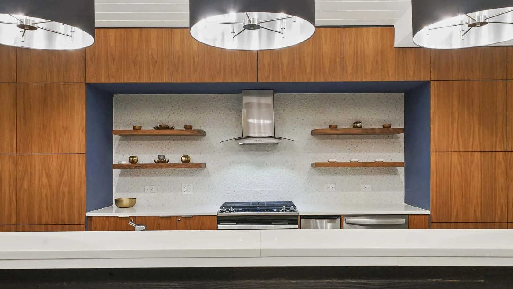 Club kitchen with statement pendants, open wood shelving, range hood, and quartz counters at 1407 on Michigan apartments in Chicago