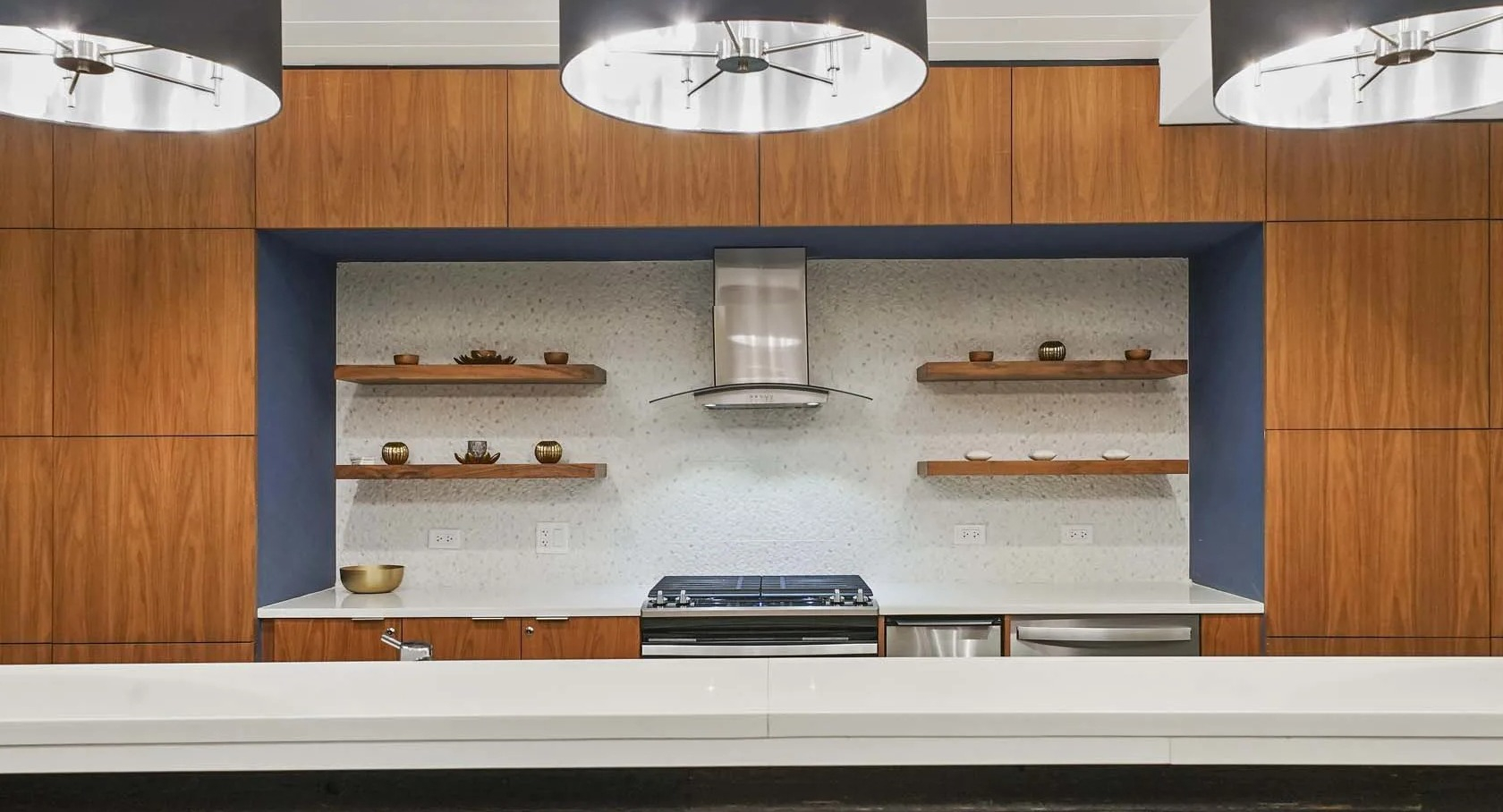 Club kitchen with statement pendants, open wood shelving, range hood, and quartz counters at 1407 on Michigan apartments in Chicago