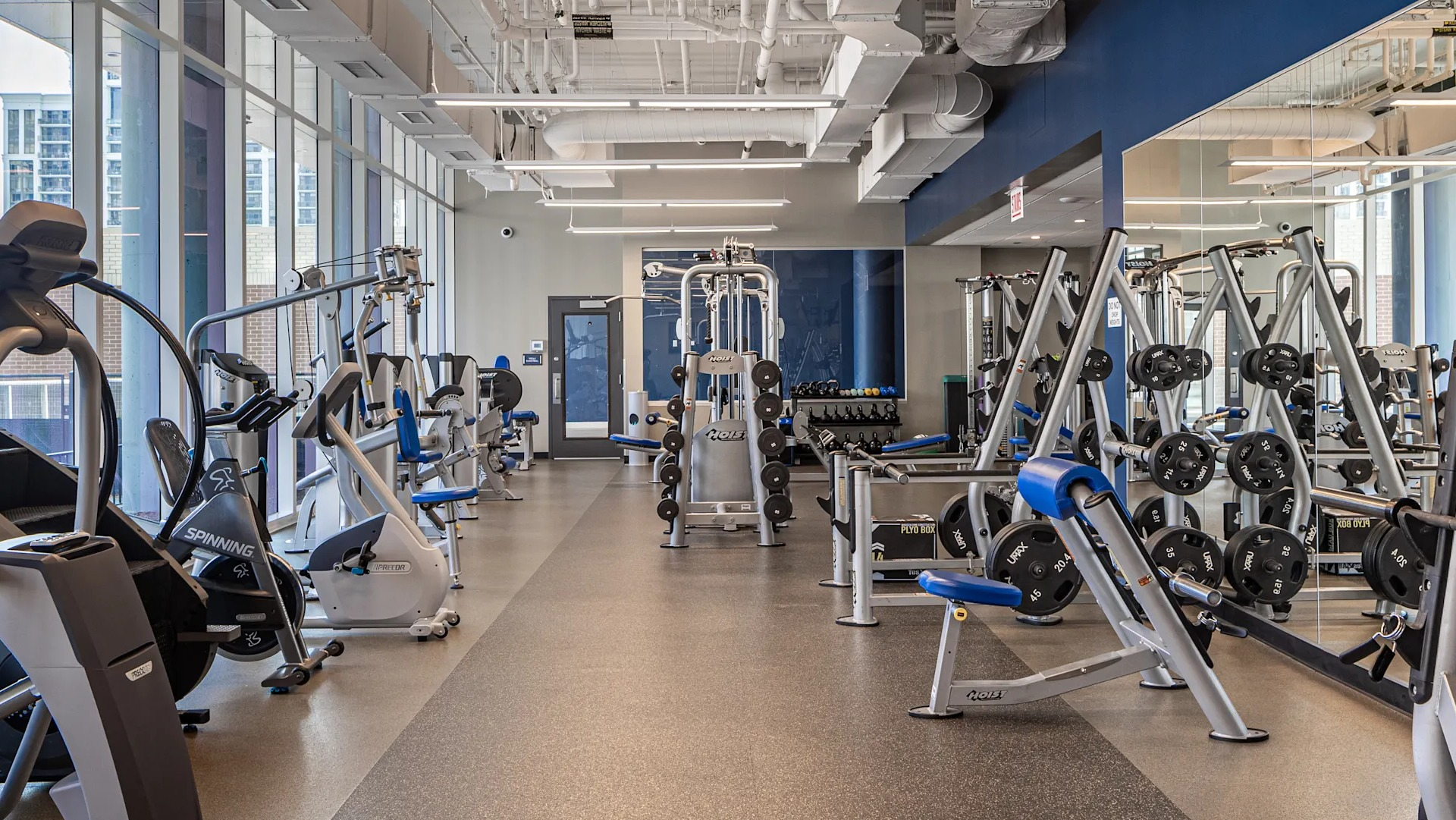 Spacious fitness center with cardio machines, strength stations, and free weights beside tall windows at 1407 on Michigan apartments in Chicago