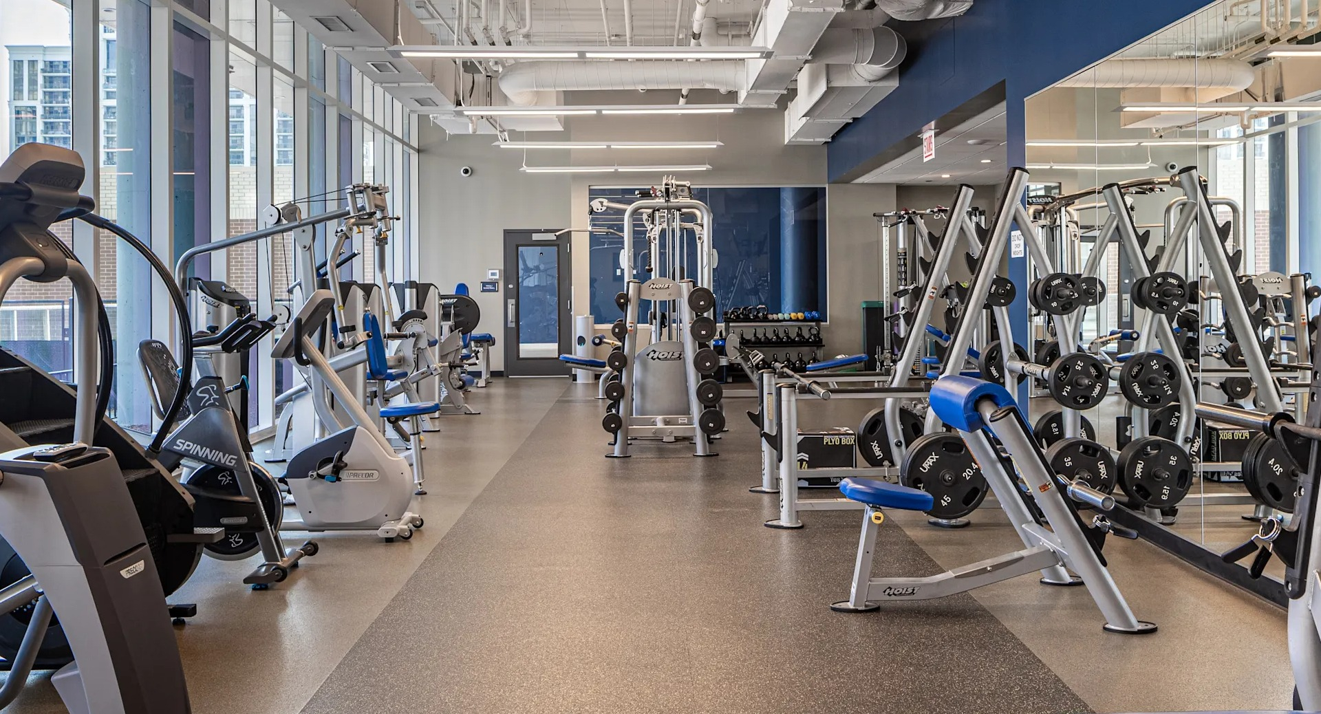 Spacious fitness center with cardio machines, strength stations, and free weights beside tall windows at 1407 on Michigan apartments in Chicago