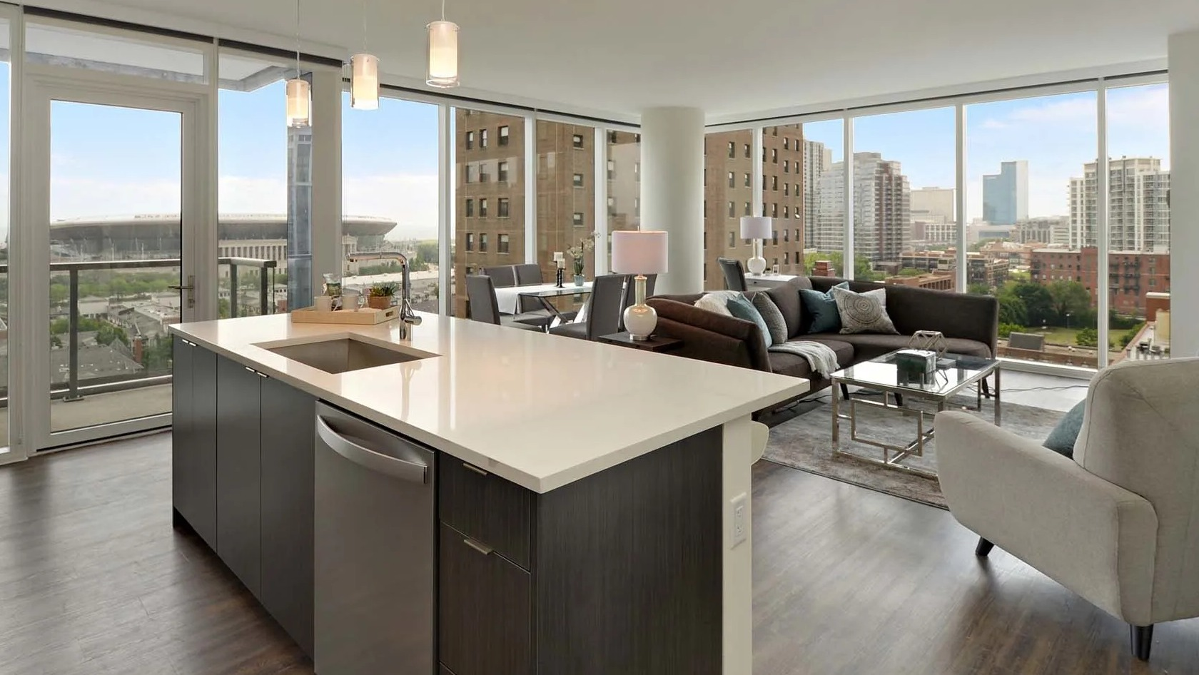 Open-concept living room and kitchen with island, floor-to-ceiling windows, balcony, and skyline views at 1407 on Michigan apartments in Chicago