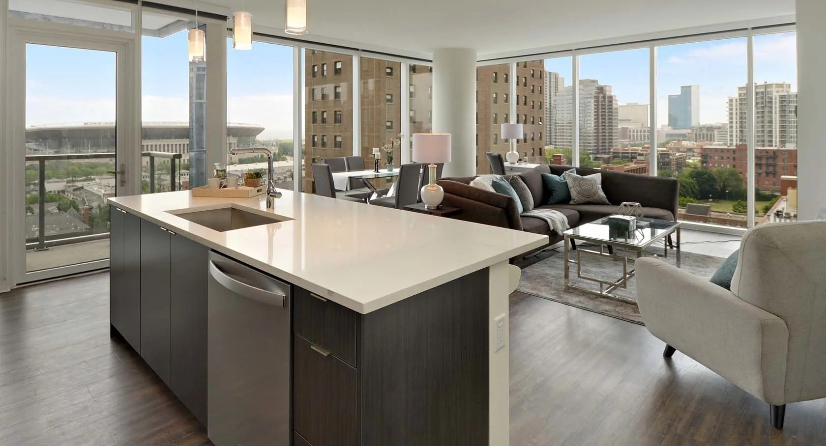 Open-concept living room and kitchen with island, floor-to-ceiling windows, balcony, and skyline views at 1407 on Michigan apartments in Chicago