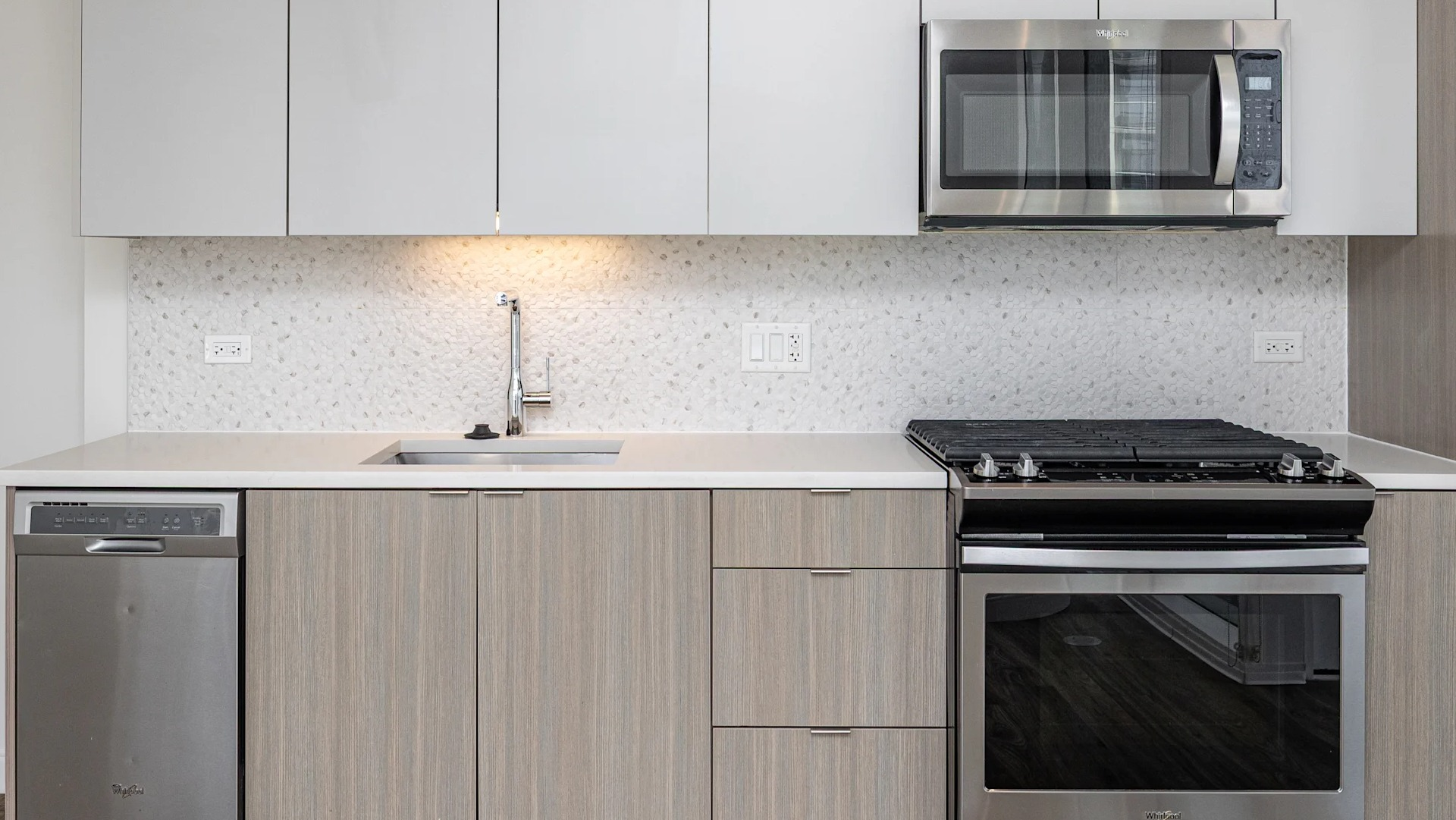 Sleek studio kitchen with light wood cabinets, gas range, microwave, dishwasher, and quartz counters at 1407 on Michigan in Chicago