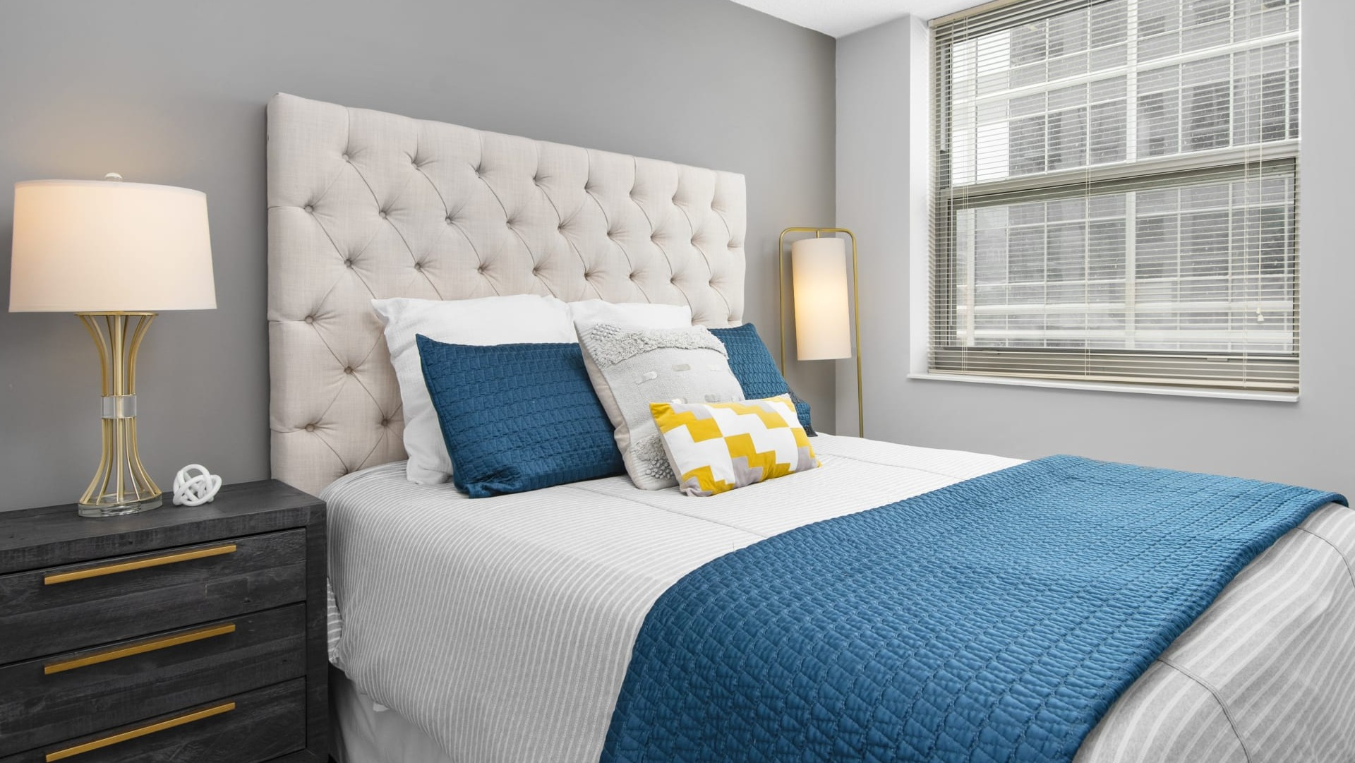 Cozy bedroom with tufted headboard, teal bedding, soft gray walls, large window and nightstands at 180 North Jefferson apartments in Chicago