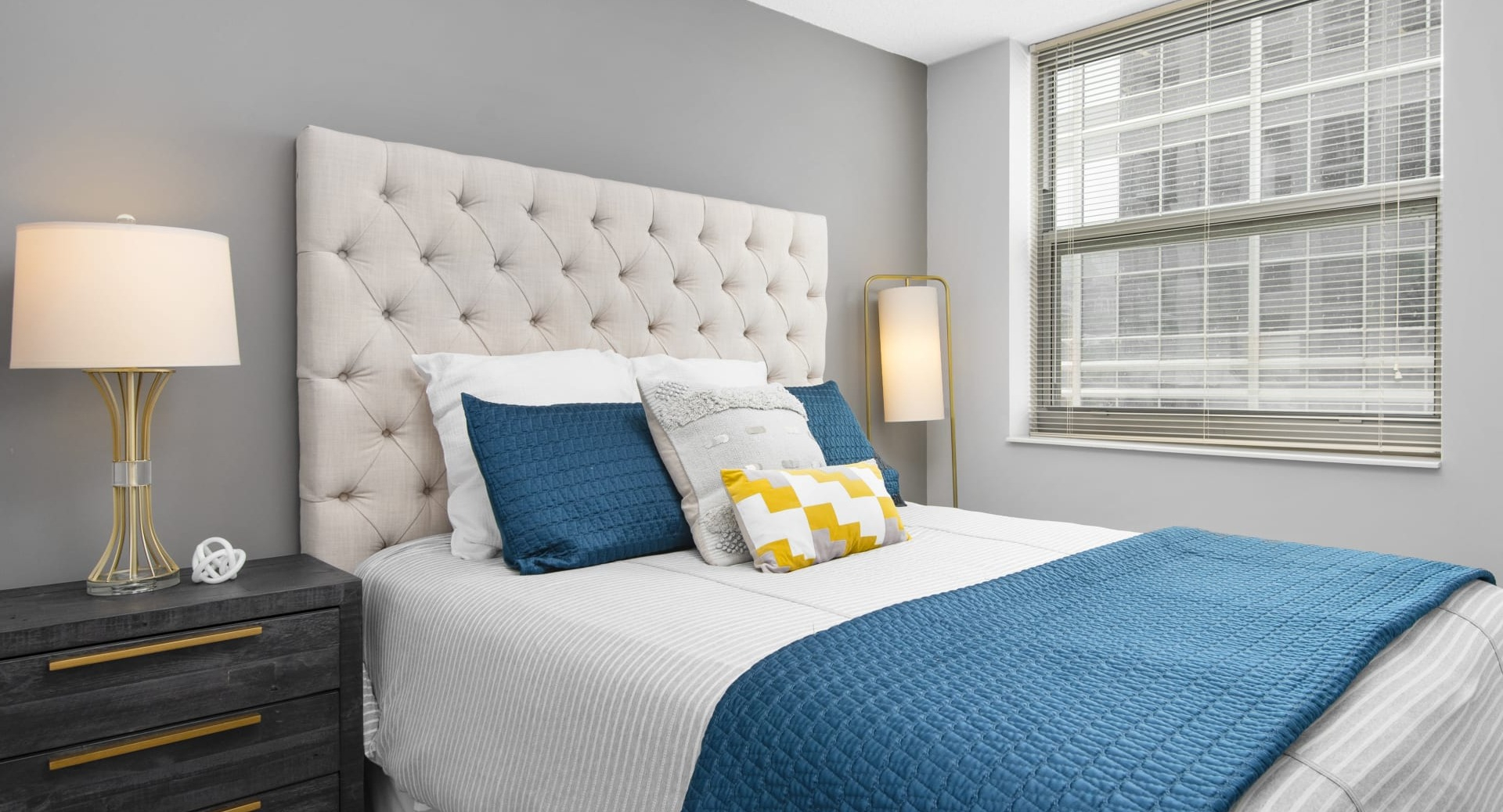 Cozy bedroom with tufted headboard, teal bedding, soft gray walls, large window and nightstands at 180 North Jefferson apartments in Chicago