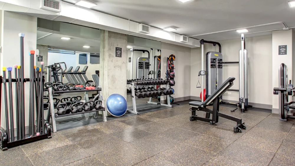 Fitness center with free weights, kettlebells, bench and mirrored walls for strength training at 180 North Jefferson apartments in Chicago