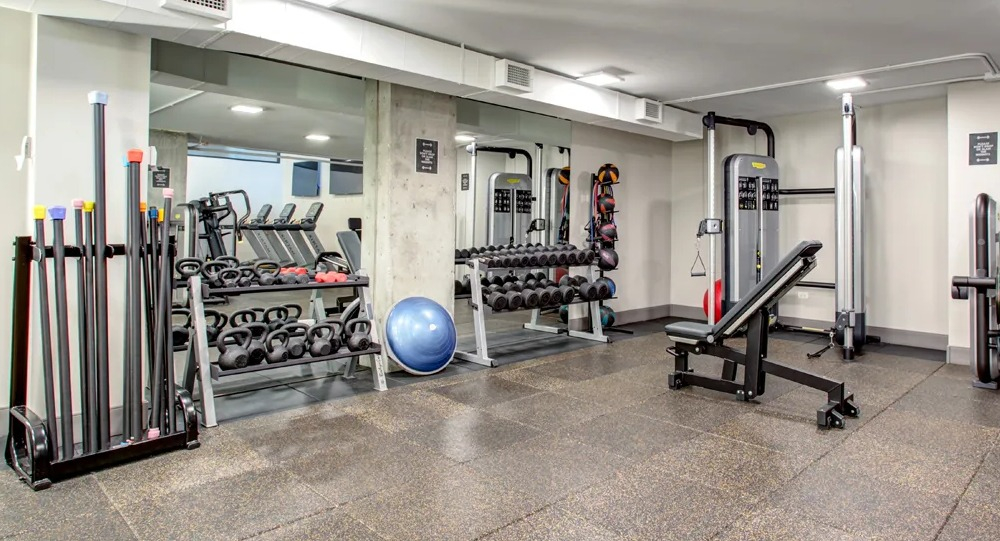 Fitness center with free weights, kettlebells, bench and mirrored walls for strength training at 180 North Jefferson apartments in Chicago