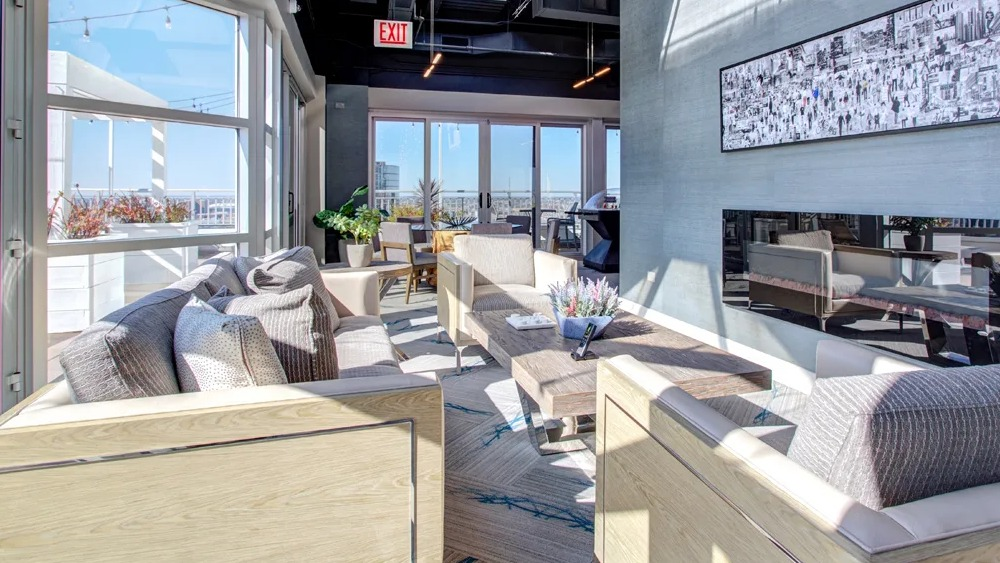 Indoor rooftop lounge with large windows, modern seating, statement lighting and a fireplace at 180 North Jefferson apartments in Chicago