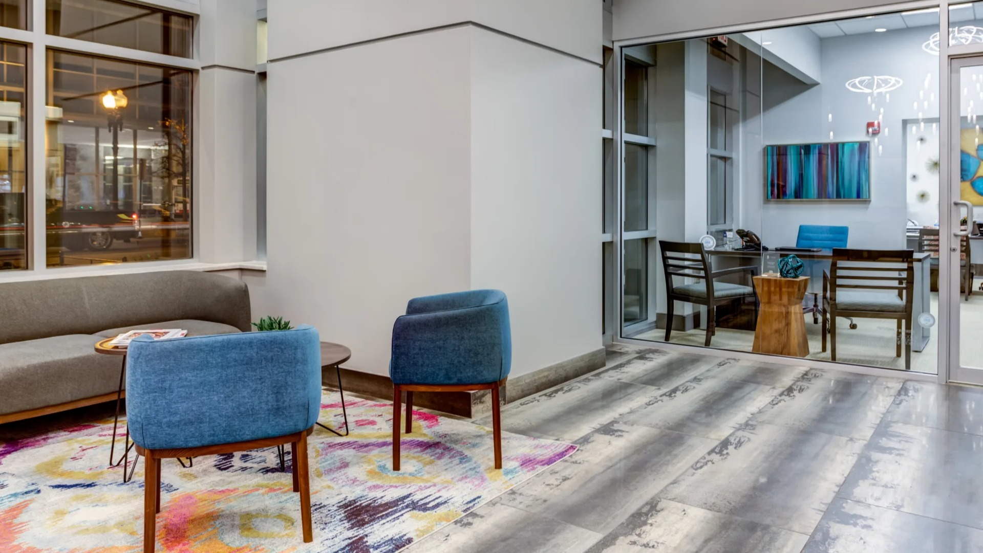 Inviting lobby seating area with modern chairs, colorful rug and a glass-walled meeting room at 180 North Jefferson apartments in Chicago