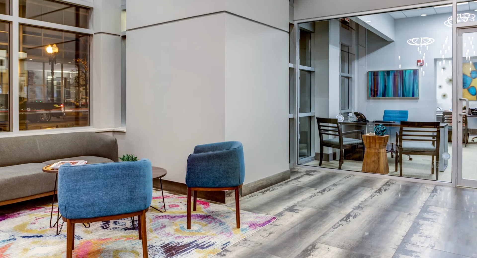 Inviting lobby seating area with modern chairs, colorful rug and a glass-walled meeting room at 180 North Jefferson apartments in Chicago