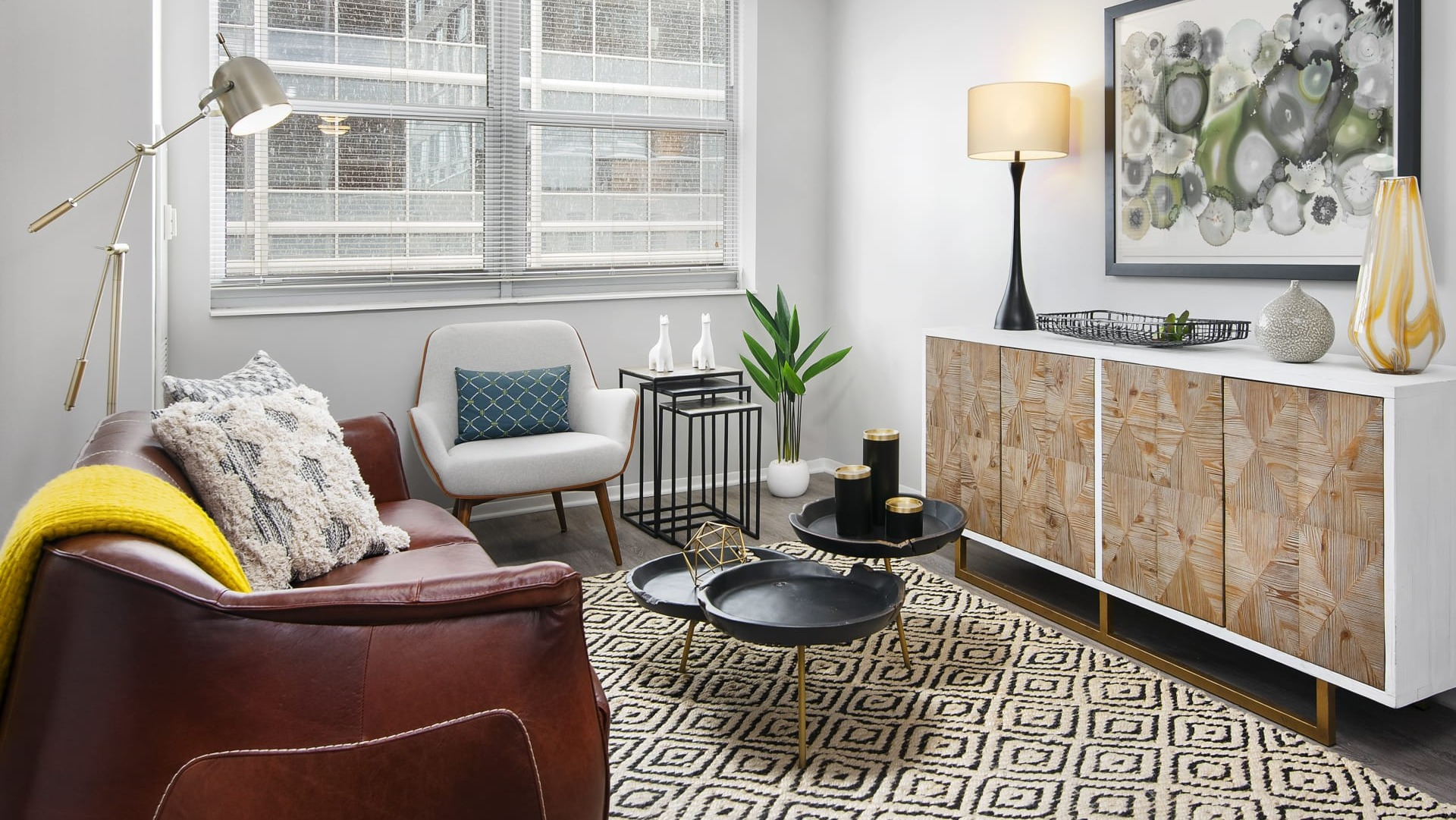 Modern living room with leather sofa, accent chair, patterned rug and wood credenza, bright windows at 180 North Jefferson apartments in Chicago