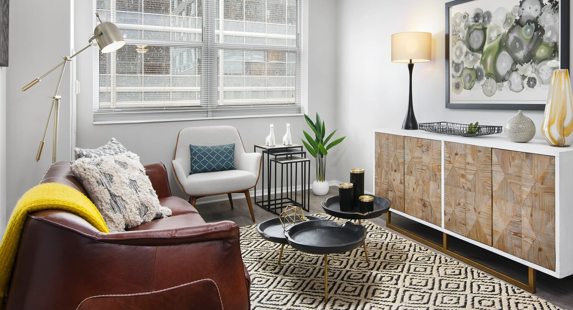 Modern living room with leather sofa, accent chair, patterned rug and wood credenza, bright windows at 180 North Jefferson apartments in Chicago