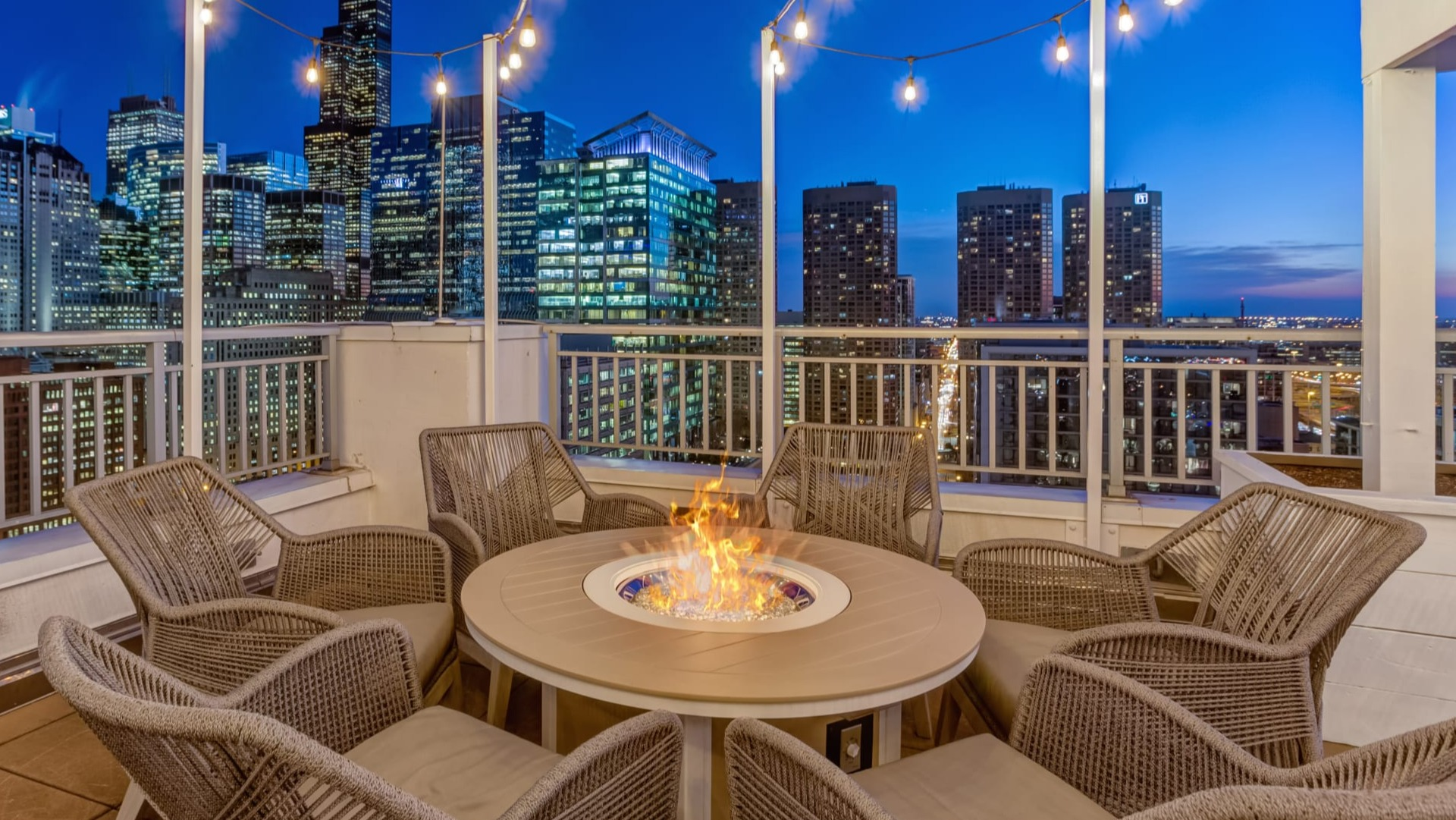 Rooftop terrace with round fire pit, wicker lounge chairs and string lights set against downtown skyline at 180 North Jefferson apartments in Chicago