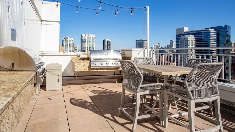 Rooftop grilling station with stainless BBQs, granite counters, bar-height dining set and string lights at 180 North Jefferson apartments in Chicago