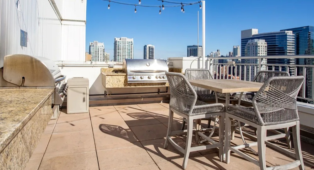 Rooftop grilling station with stainless BBQs, granite counters, bar-height dining set and string lights at 180 North Jefferson apartments in Chicago