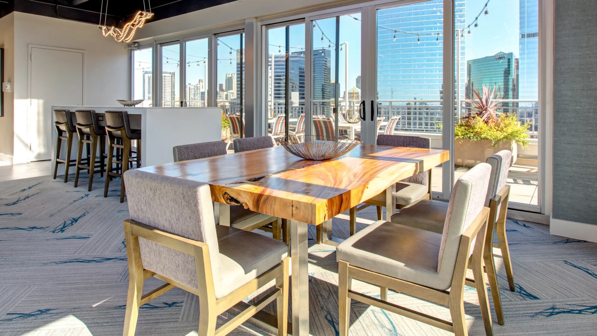 Skyline-view rooftop lounge with live-edge dining table, pendant lights, and sliding doors to an outdoor terrace at 180 North Jefferson apartments in Chicago