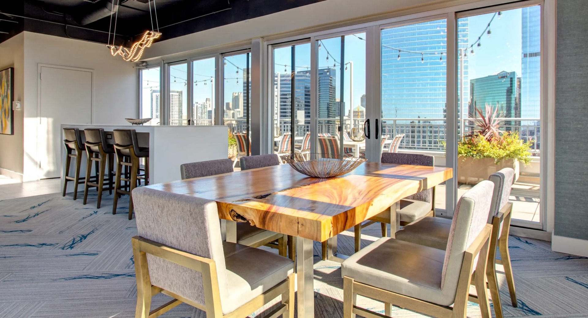 Skyline-view rooftop lounge with live-edge dining table, pendant lights, and sliding doors to an outdoor terrace at 180 North Jefferson apartments in Chicago