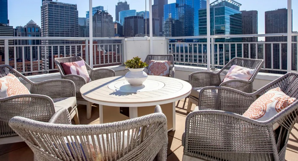 Rooftop lounge seating with round table, woven chairs and skyline views under bistro lights at 180 North Jefferson apartments in Chicago