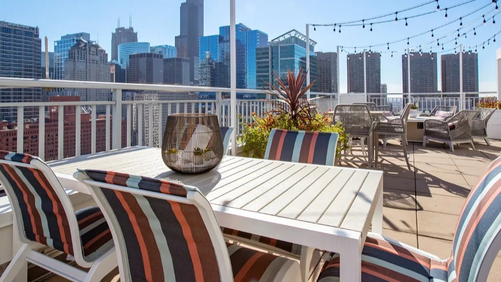 Skyline terrace with outdoor dining table, striped chairs and cafe lights near Willis Tower at 180 North Jefferson apartments in Chicago