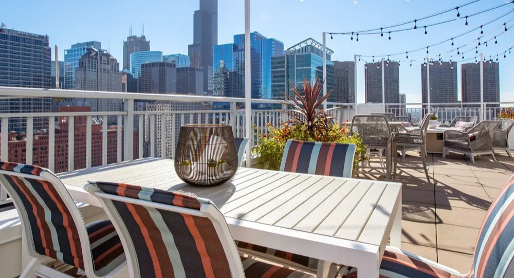 Skyline terrace with outdoor dining table, striped chairs and cafe lights near Willis Tower at 180 North Jefferson apartments in Chicago