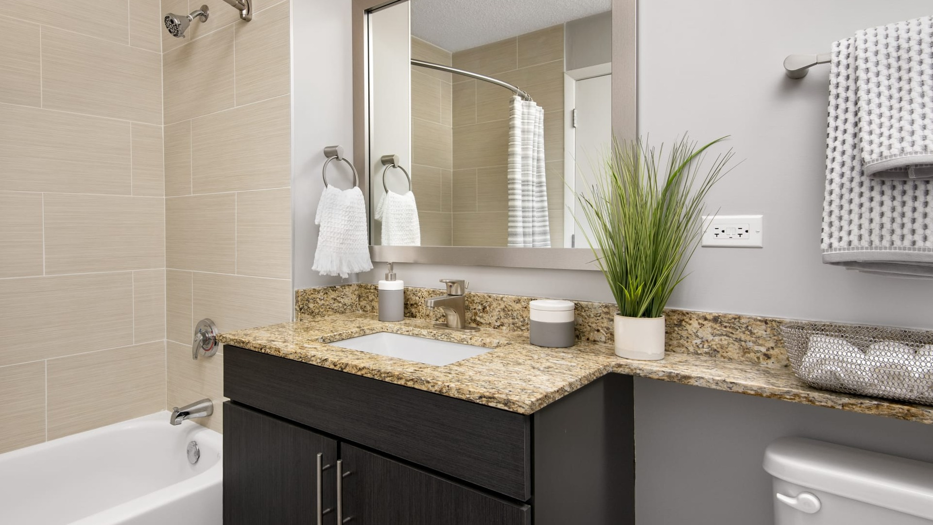 Updated bathroom with granite vanity, large mirror, tiled tub-shower and neutral finishes at 180 North Jefferson apartments in Chicago