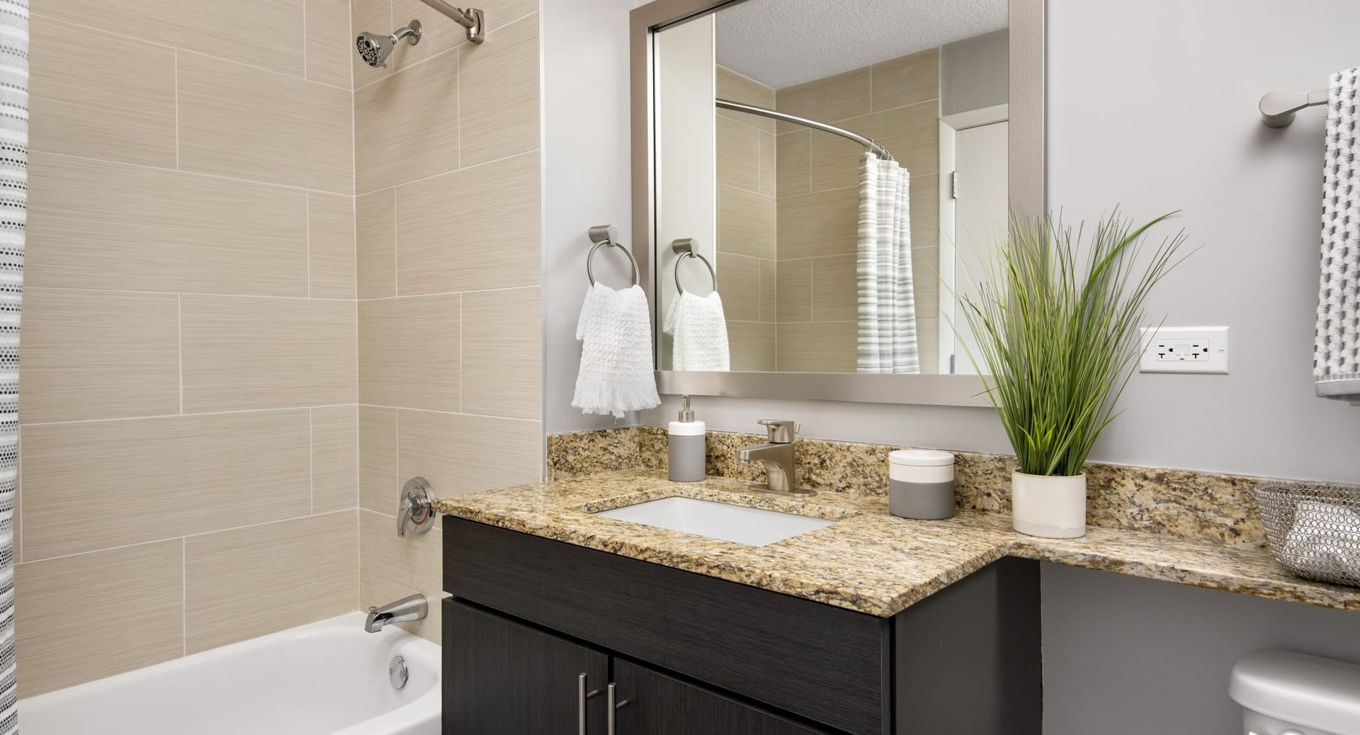 Updated bathroom with granite vanity, large mirror, tiled tub-shower and neutral finishes at 180 North Jefferson apartments in Chicago