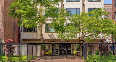 Gated boutique apartment building with mature trees, brick neighbors, and large windows at 20 E Scott apartments in Chicago