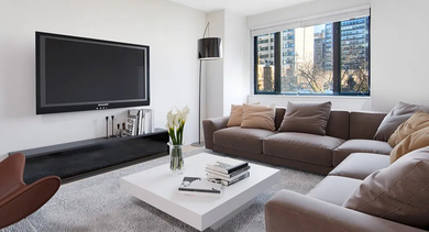 Spacious living room with a large sectional sofa, wall-mounted TV, big window, and neutral décor at 20 E Scott apartments in Chicago