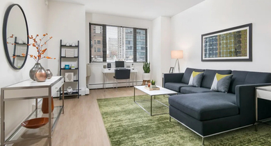 Spacious living room with sectional sofa, green area rug, side tables, and a bright desk nook by the window at 20 E Scott apartments in Chicago