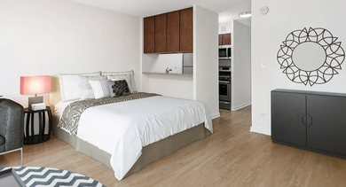 Studio sleeping area with queen bed, nightstand, soft lighting, and a nearby pass-through kitchen at 20 E Scott apartments in Chicago