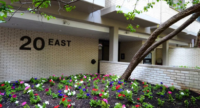 Welcoming entry with landscaped flower beds, light brick façade, and bold “20 East” signage at 20 E Scott apartments in Chicago