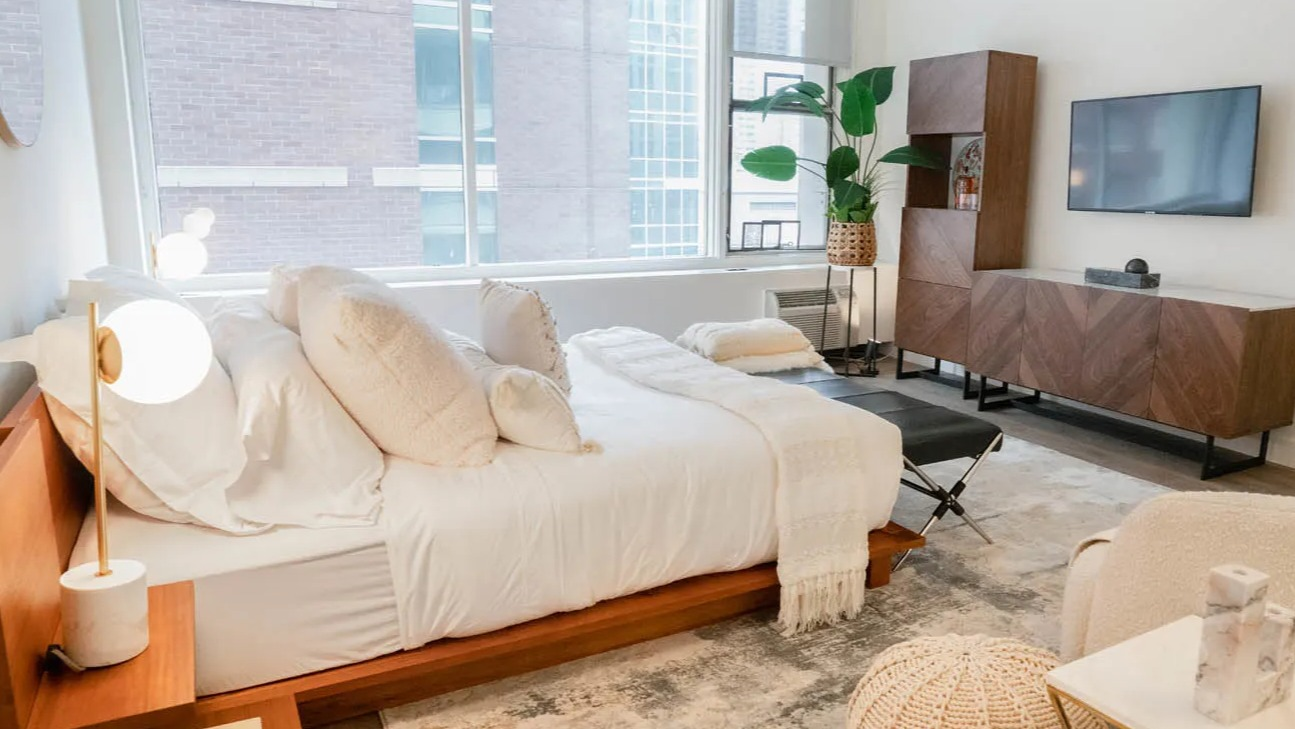 Airy studio bedroom with bedside globe lamps, textured rug, and modern media wall at 21 E Chestnut apartments in Chicago