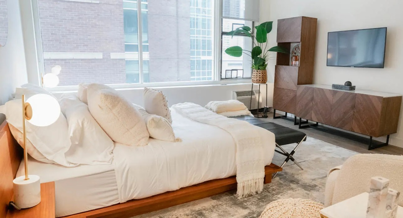 Airy studio bedroom with bedside globe lamps, textured rug, and modern media wall at 21 E Chestnut apartments in Chicago