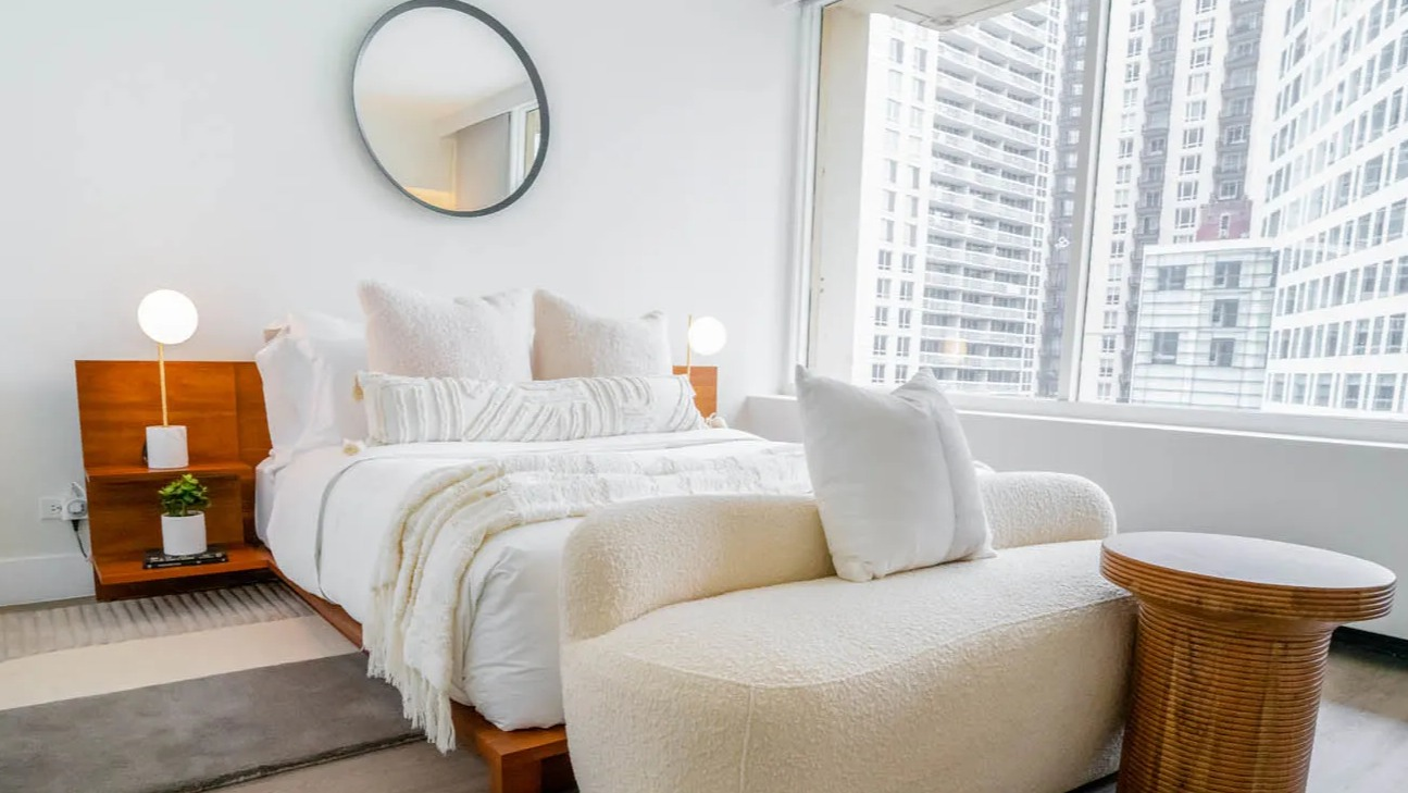 Bright bedroom with large window, wood platform bed, boucle loveseat, and city views at 21 E Chestnut apartments in Chicago