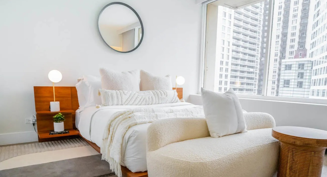 Bright bedroom with large window, wood platform bed, boucle loveseat, and city views at 21 E Chestnut apartments in Chicago