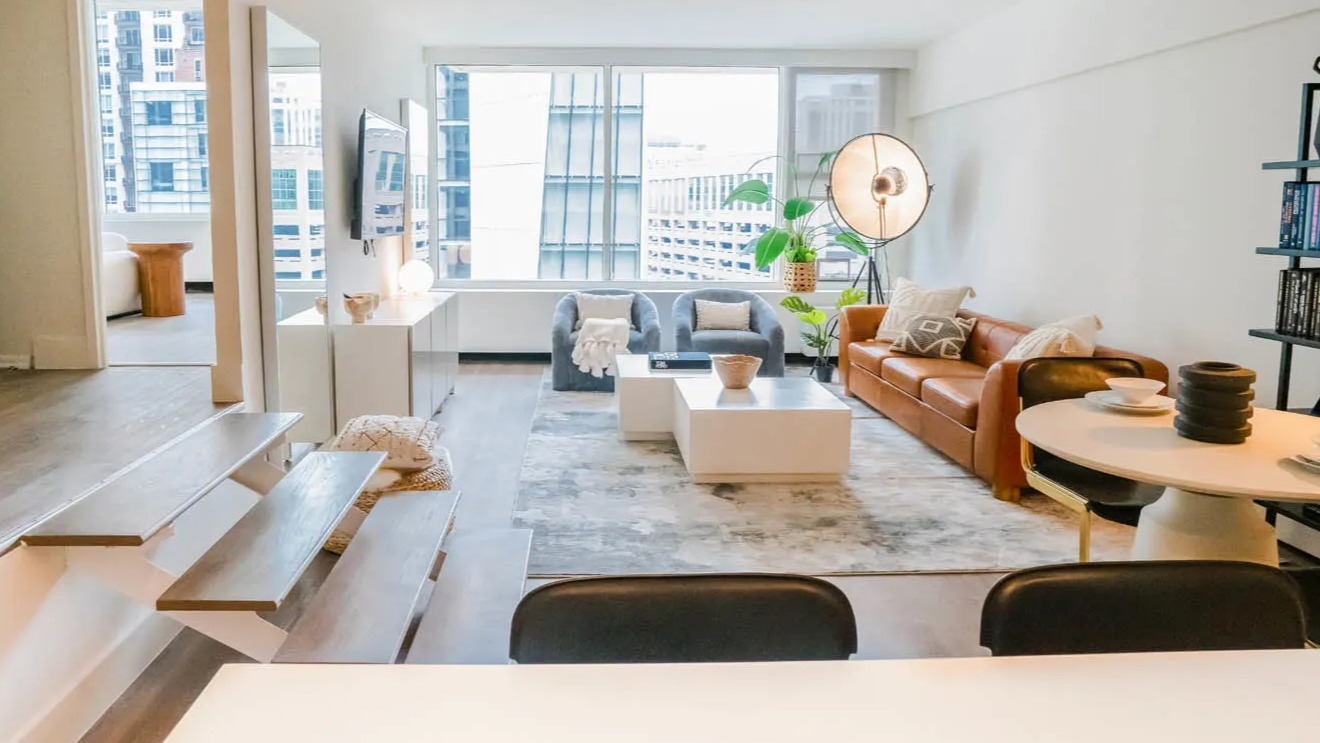 Bright step-down living room with floating stairs, white media console, and city views at 21 E Chestnut apartments in Chicago