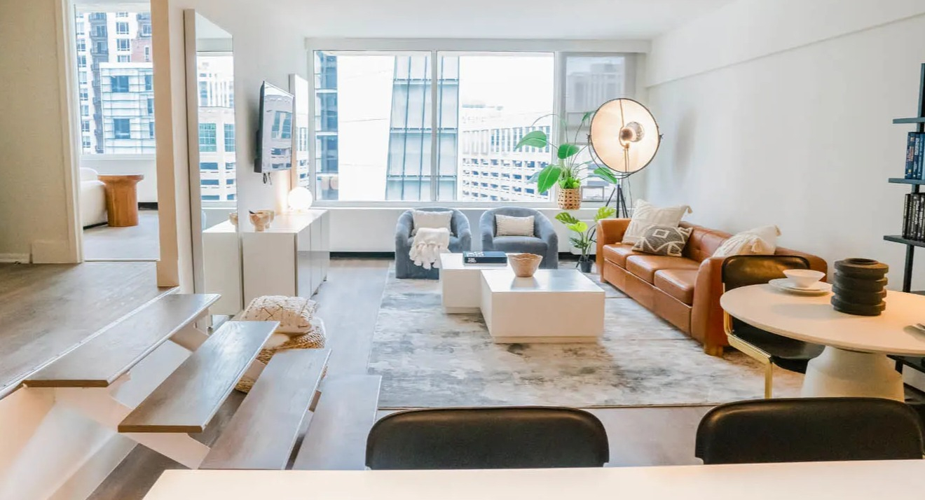 Bright step-down living room with floating stairs, white media console, and city views at 21 E Chestnut apartments in Chicago