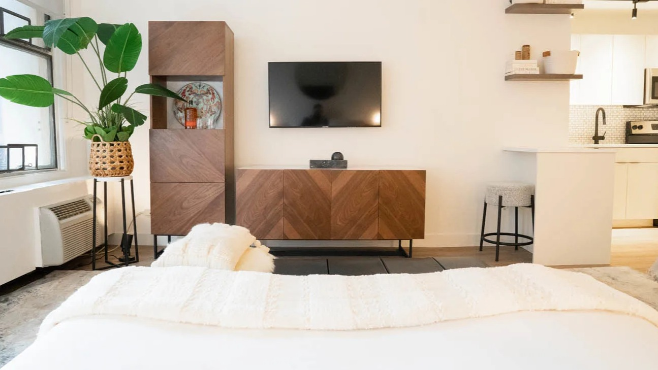Cozy studio with bed, wood media console, wall-mounted TV, and breakfast counter by a bright window at 21 E Chestnut apartments in Chicago