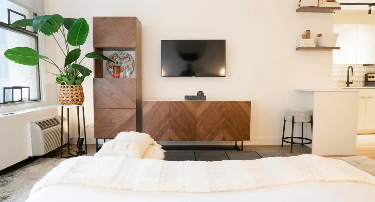 Cozy studio with bed, wood media console, wall-mounted TV, and breakfast counter by a bright window at 21 E Chestnut apartments in Chicago