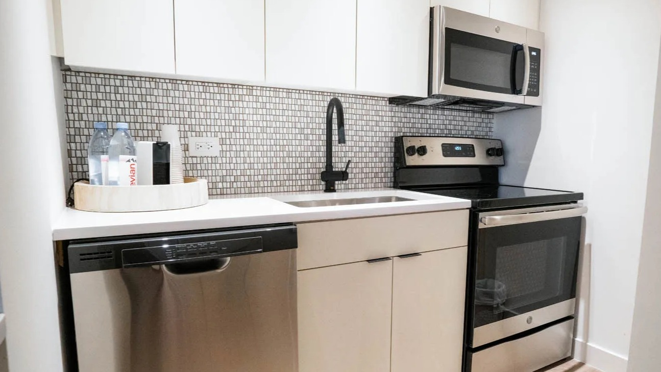 Modern galley kitchen with white cabinets, mosaic backsplash, black pull-down faucet, and stainless appliances at 21 E Chestnut apartments in Chicago