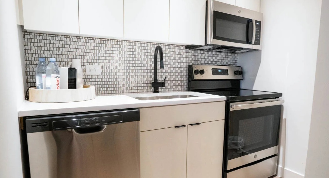 Modern galley kitchen with white cabinets, mosaic backsplash, black pull-down faucet, and stainless appliances at 21 E Chestnut apartments in Chicago