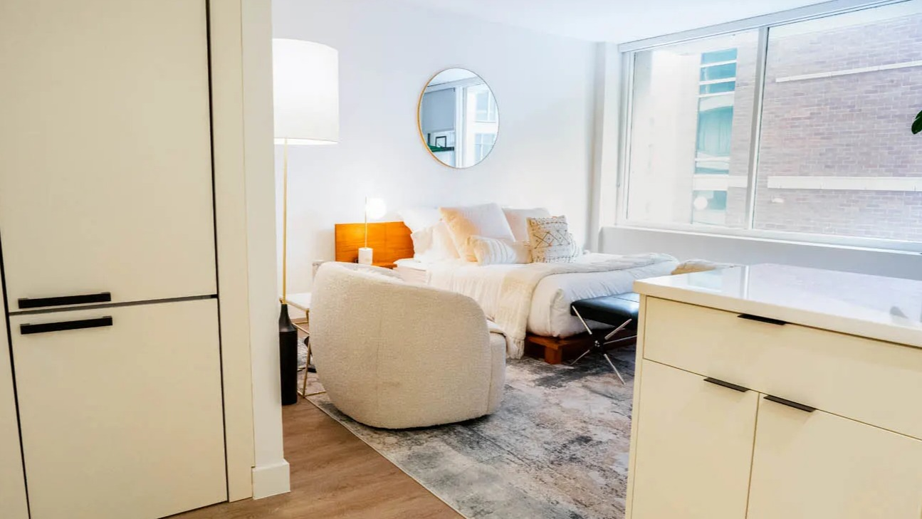 Open-concept studio with cozy bed, boucle chair, and wide window bringing natural light at 21 E Chestnut apartments in Chicago