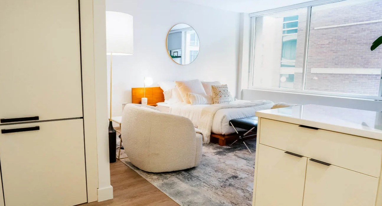 Open-concept studio with cozy bed, boucle chair, and wide window bringing natural light at 21 E Chestnut apartments in Chicago