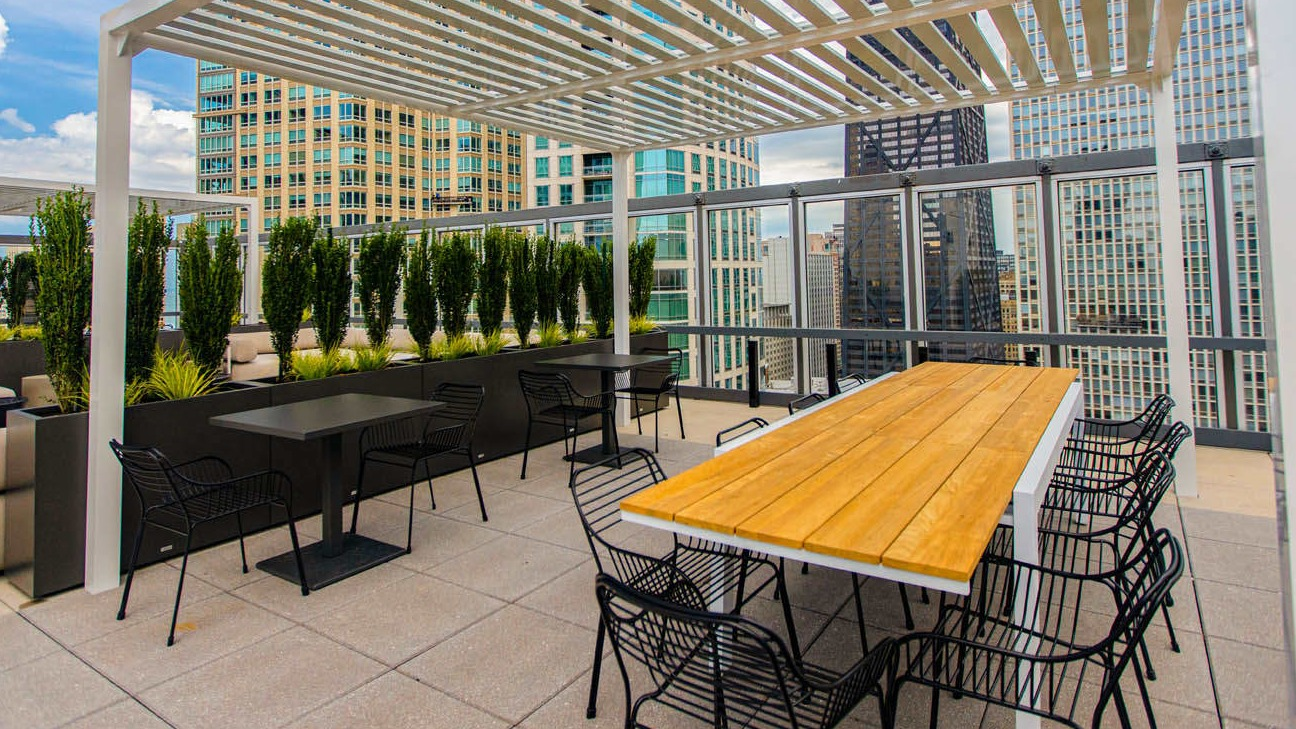 Rooftop dining area under a modern pergola with long wood table, ample seating, and skyline views at 21 E Chestnut apartments in Chicago