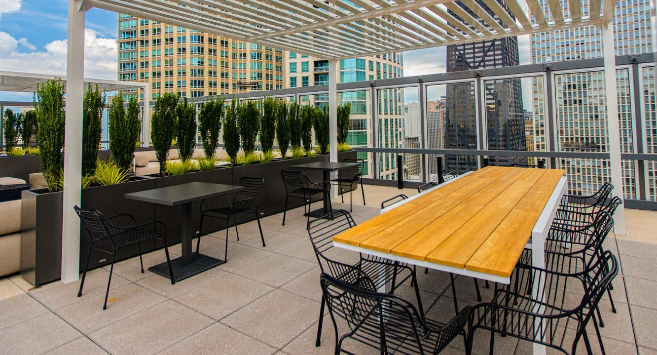 Rooftop dining area under a modern pergola with long wood table, ample seating, and skyline views at 21 E Chestnut apartments in Chicago