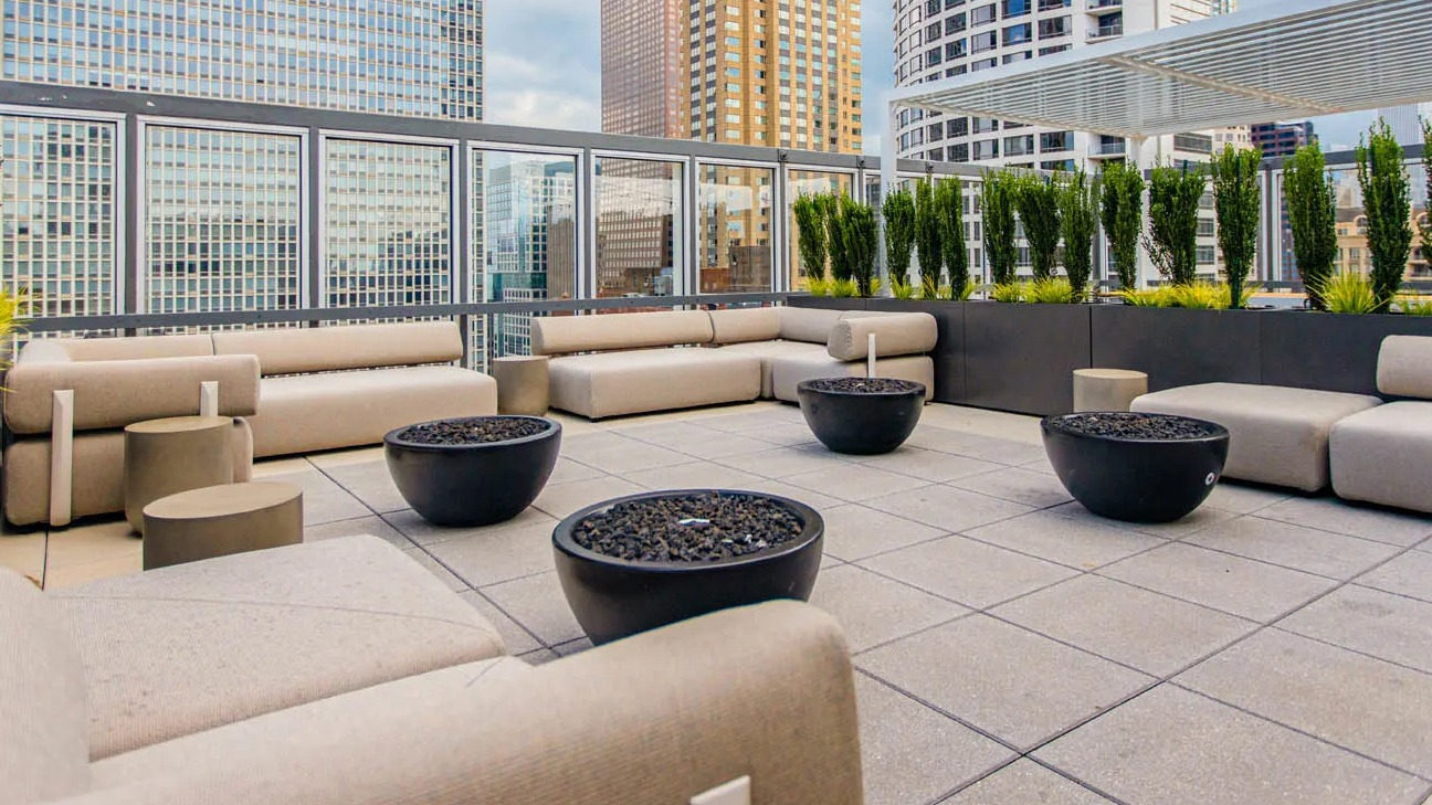 Rooftop lounge with cushioned sofas, round fire pits, greenery planters, and open city views at 21 E Chestnut apartments in Chicago