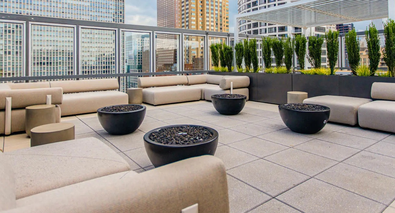 Rooftop lounge with cushioned sofas, round fire pits, greenery planters, and open city views at 21 E Chestnut apartments in Chicago
