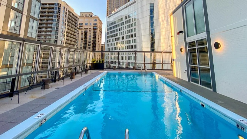 Sunlit rooftop pool bordered by glass railings and lounge seating, surrounded by high-rises at 21 E Chestnut apartments in Chicago