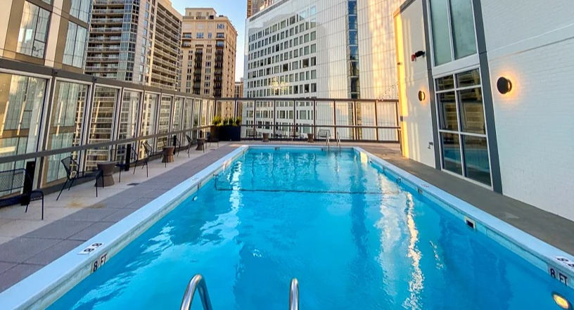 Sunlit rooftop pool bordered by glass railings and lounge seating, surrounded by high-rises at 21 E Chestnut apartments in Chicago